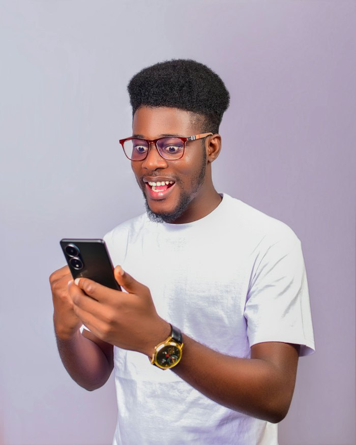 A young Black man in glasses smiling at his phone