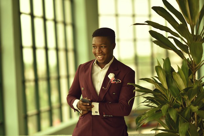 A smiling Nigerian man in a suit holding his phone