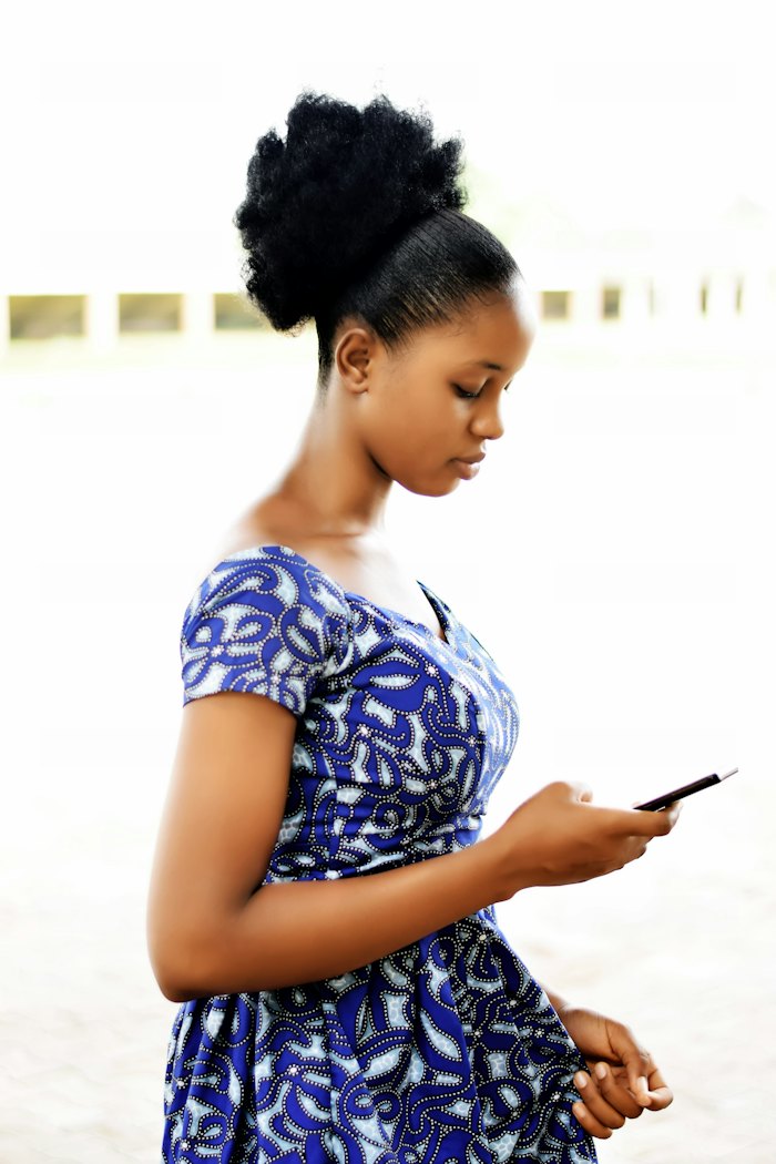 A young Nigerian woman in a blue ankara dress checking her phone